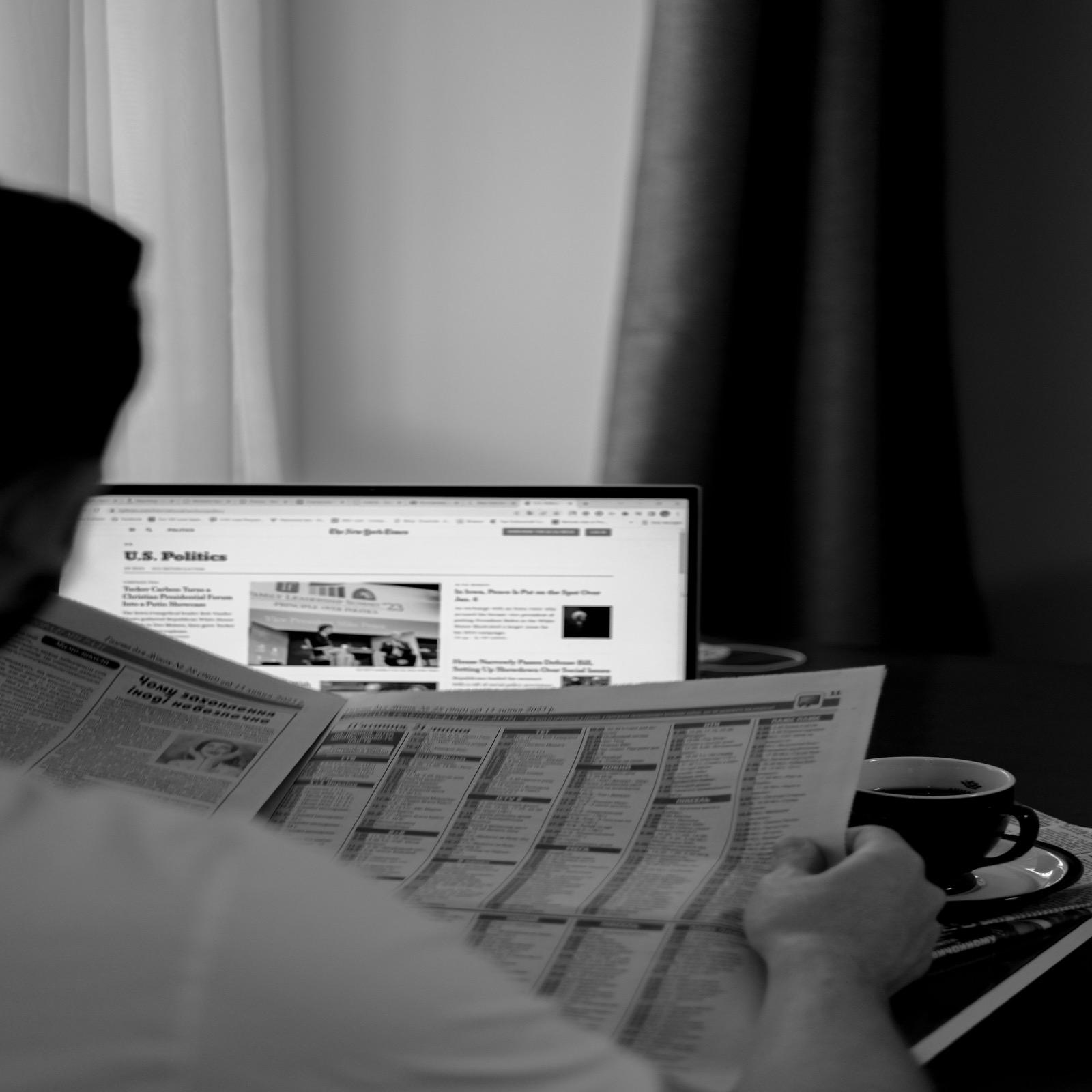 Person reading a newspaper next to a laptop showing the news